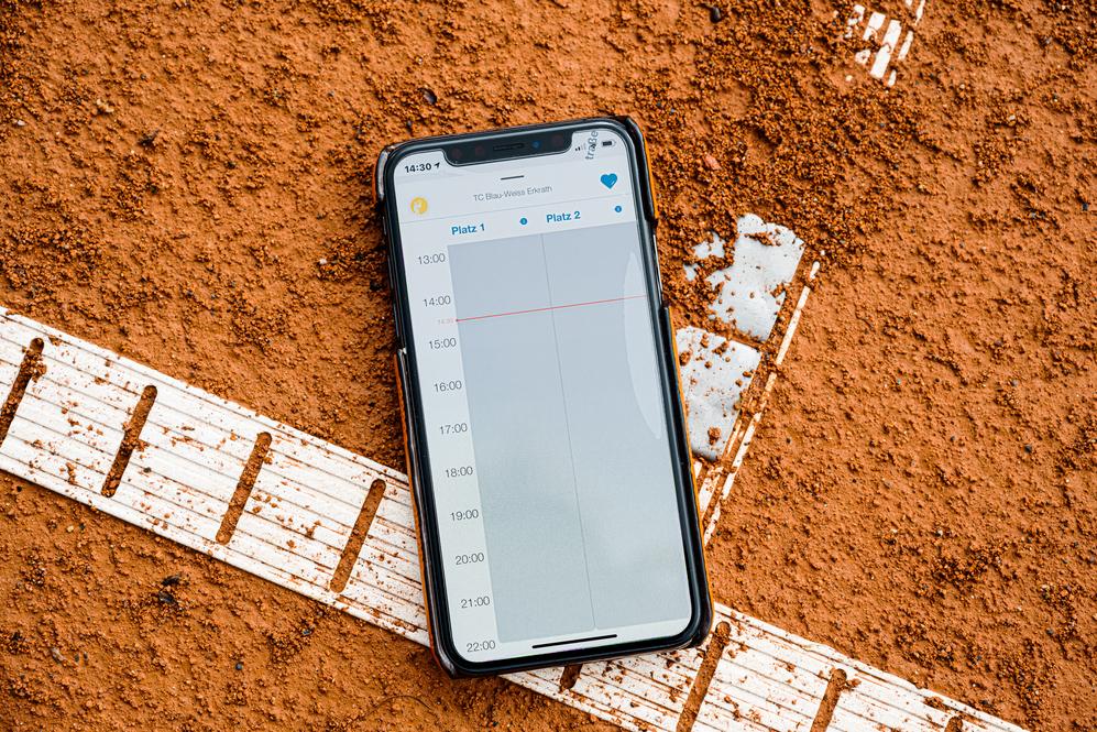 Smartphone auf rotem Tennisplatz, zeigt den Wochenplan mit Zeiten für zwei Plätze.