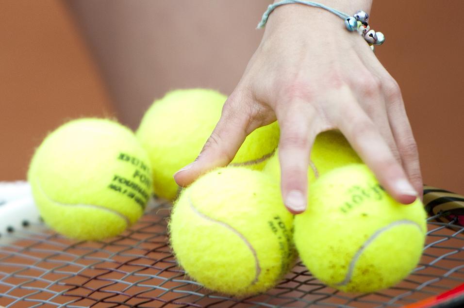 Hand greift mehrere gelbe Tennisbälle auf einem Tennisschläger, während die andere Hand die Schlägerhaltung stabilisiert.