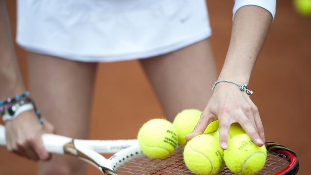 Hand greift mehrere gelbe Tennisbälle auf einem Tennisschläger, während die andere Hand die Schlägerhaltung stabilisiert.